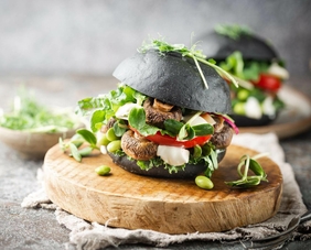 Vegetarischer Burger im schwarzen Brötchen, mit saftigen Pilzen, frischem Rucola und Sojabohnen