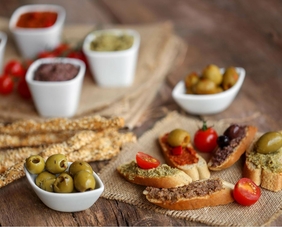 Eine Schüssel mit Oliven und Baguettestückchen, begleitet von einer Vielzahl von Antipasti-Spezialitäten und Cherrytomaten