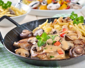 Gebratenes Fleisch, frische Champignons und eine helle Sauce, dazu knusprige Pommes Frites, serviert in einer Pfanne