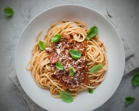 Spaghetti serviert auf einem weißen Teller und garniert mit frischem Basilikumblättern