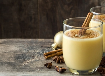 zwei Gläser Eggnog auf einem Holztisch mit Zimtstangen