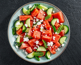 Eine Schüssel mit frisch geschnittenen Gurken und Tomaten, garniert mit Balkankäse